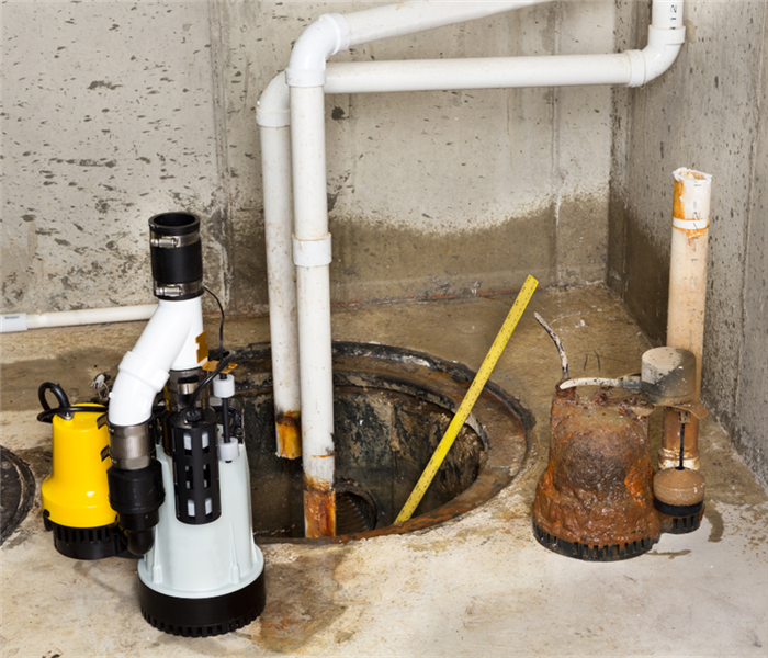 Picture shows a sump pump is a basement with the lid off. There are tools all around the sump. 