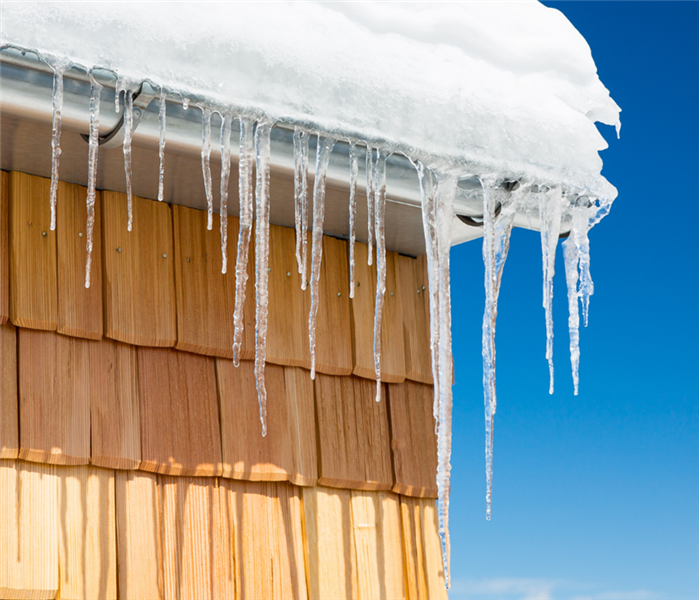 Picture is of a roof covered in snow with icicles hanging out of the gutter. 