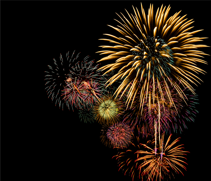 Yellow, green, and purple fireworks are scattered across a night sky.