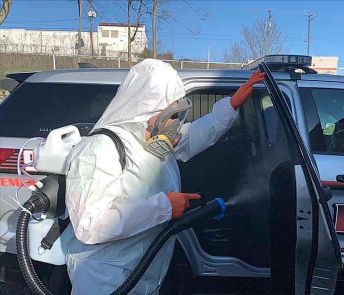 image of SERVPRO worker in full PPE misting the inside of a Police vehicle